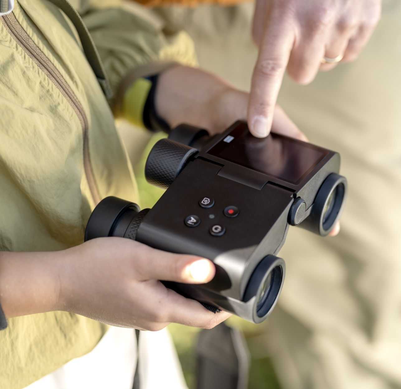 Hands holding and operating Solvia ED 8x32 digital binoculars with touchscreen display outdoors
