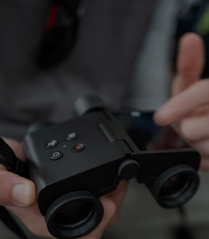 Close-up of a person holding a black Solvia ED 8x32 binoculars with a blurred background